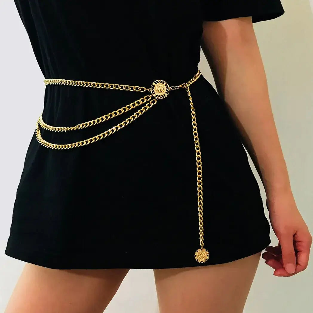 Cinto Feminino Corrente de Metal dourado usado sobre vestido preto curto, com três fios drapeados e pingente medalha