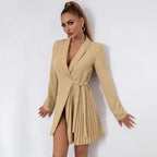 Vestido Blazer Curto Plissado Bege visto de frente, com decote transpassado, faixa de amarração e saia plissada lateral