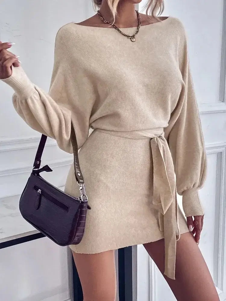 Vestido Curto de Malha com Manga Bufante e Gola Canoa bege, com colar dourado, faixa na cintura e bolsa marrom a tiracolo