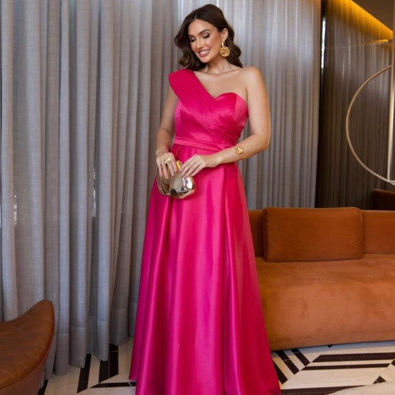 Vestido de Festa Longo Acetinado Um Ombro Só na cor pink, visto de frente com clutch metalizada e drapeado no busto