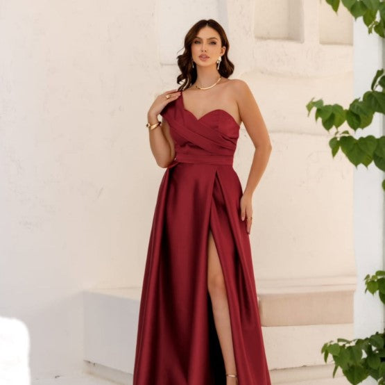 Vestido de Festa Longo Acetinado Um Ombro Só na cor vinho, em cena externa com fenda frontal e colar de pérolas