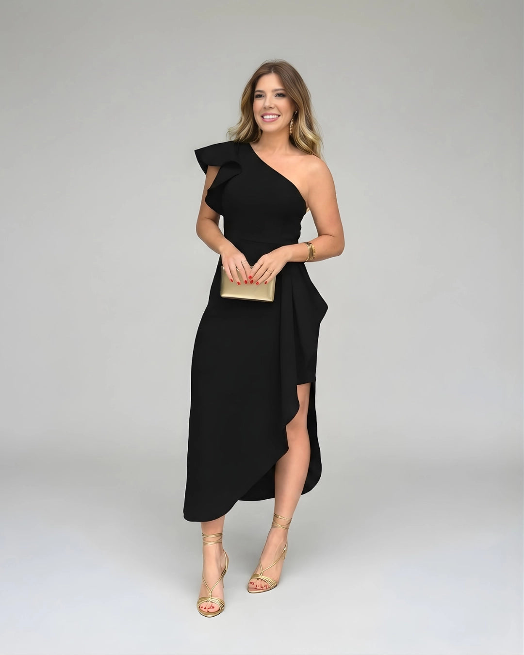 Vestido de Festa Longo Preto Um Ombro Só visto de frente, com clutch dourada na altura da cintura e sandália nude de amarração