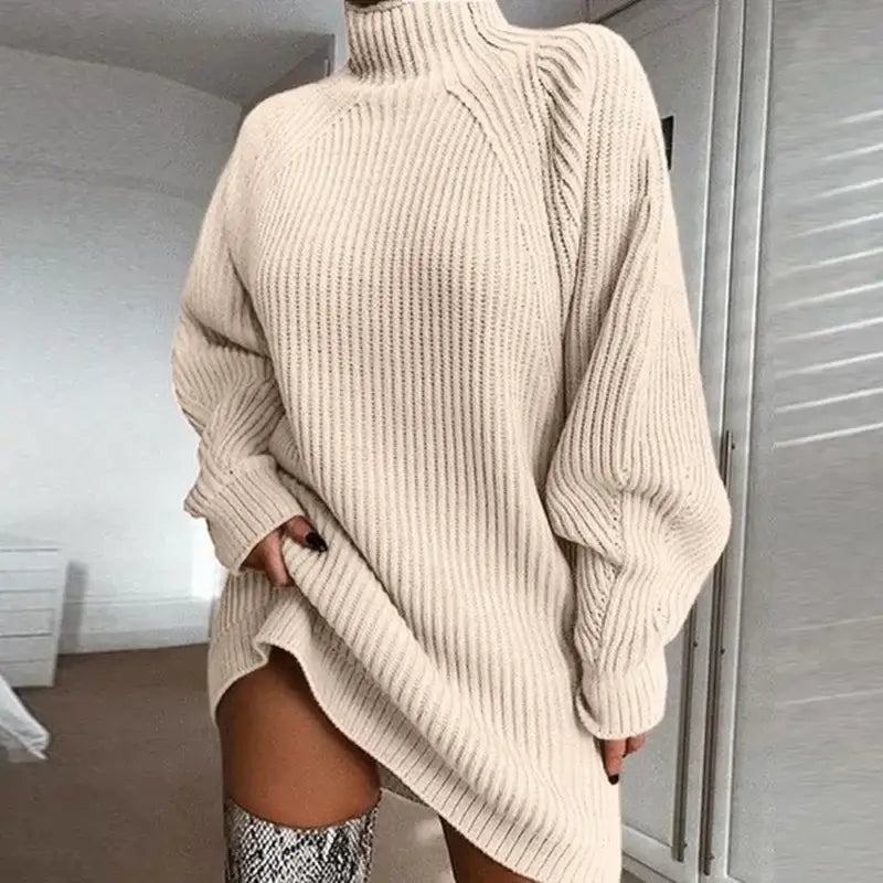 Vestido de Tricot Oversized Gola Alta Bege em plano de meio corpo, com a mão no bolso e bota de cano alto