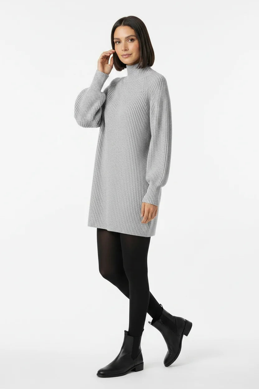 Vestido de Tricot Oversized Gola Alta Cinza em pose de três quartos, com a mão junto ao rosto e mangas amplas