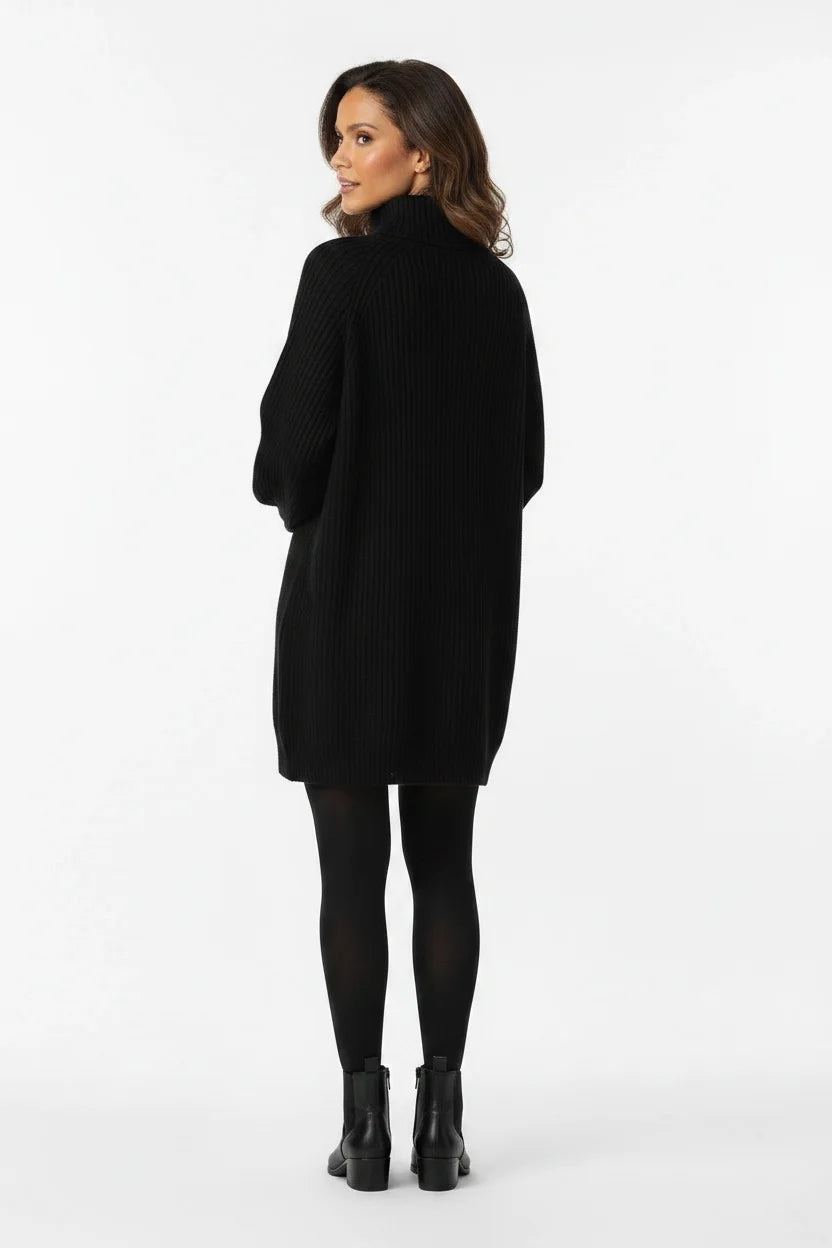 Vestido de Tricot Oversized Gola Alta Preto visto de costas, com o caimento amplo da malha e bota tratorada