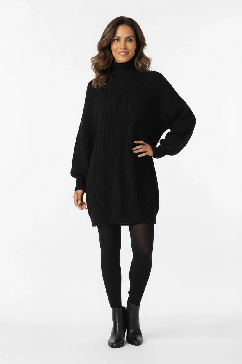 Vestido de Tricot Oversized Gola Alta Preto em pose de três quartos, modelo sorrindo com a mão na cintura