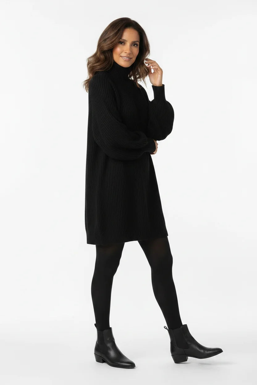 Vestido de Tricot Oversized Gola Alta Preto de frente, com a mão junto ao rosto e mangas bufantes