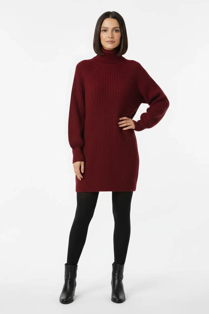 Vestido de Tricot Oversized Gola Alta Vinho visto de frente, com a mão na cintura, meia-calça preta e bota de cano curto