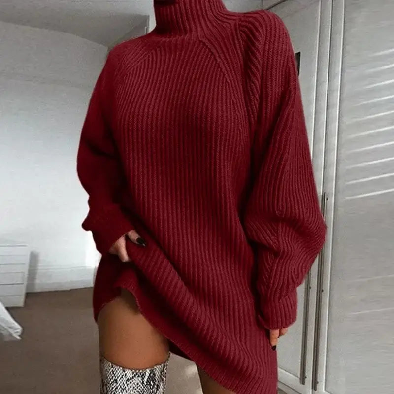 Vestido de Tricot Oversized Gola Alta Vinho em plano aproximado, com a mão puxando a barra e bota de cano alto