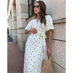 Vestido Feminino Midi Florido Amarelo em pose encostada na parede, com óculos escuros e bolsa de palha