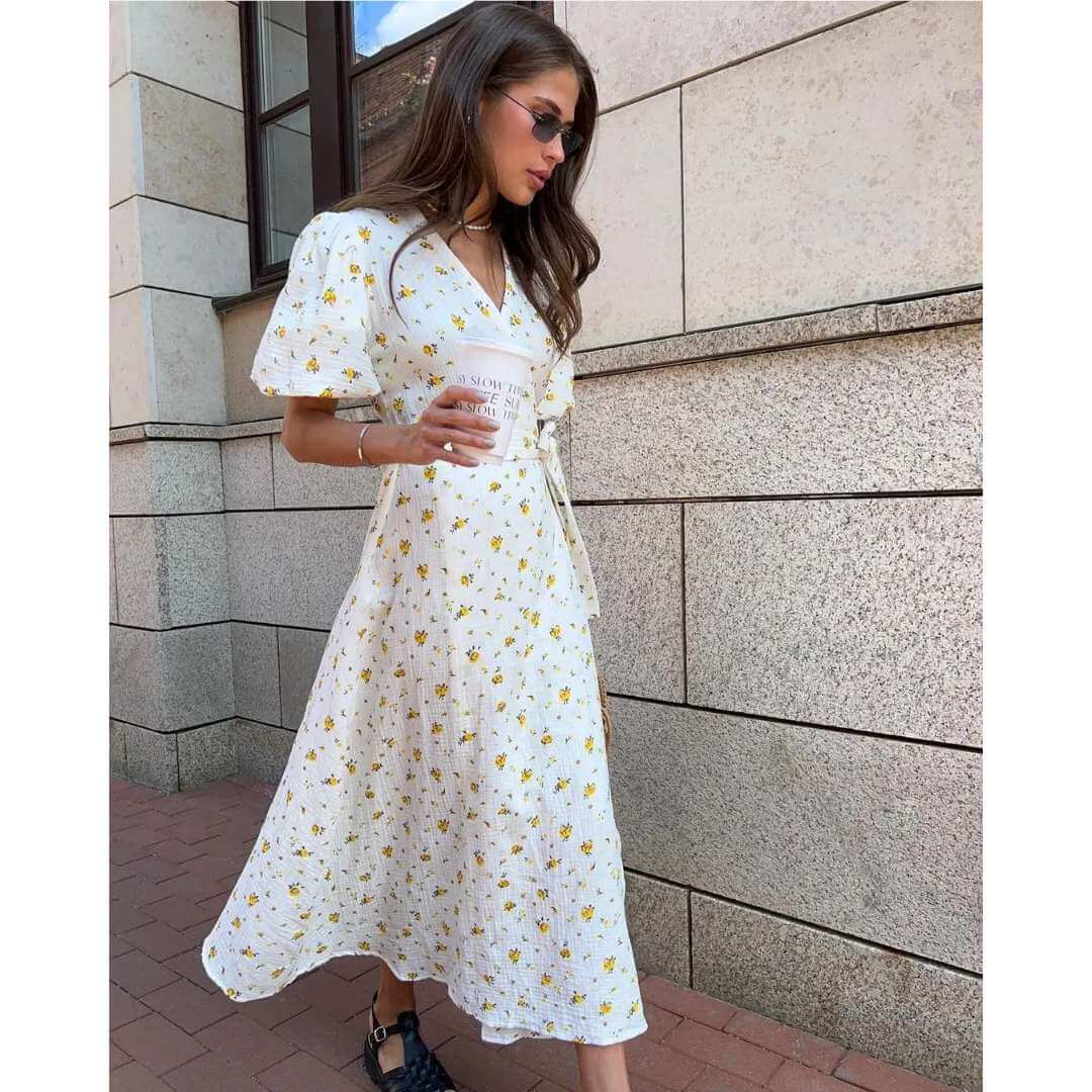 Vestido Feminino Midi Florido Amarelo em movimento na calçada, com a saia transpassada abrindo na perna