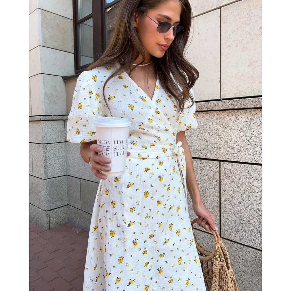 Vestido Feminino Midi Florido Amarelo em plano aproximado, com copo de café na mão e colar delicado