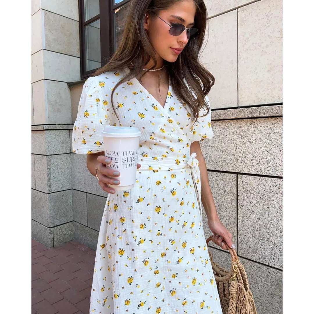 Vestido Feminino Midi Florido Amarelo em plano aproximado, com copo de café na mão e colar delicado