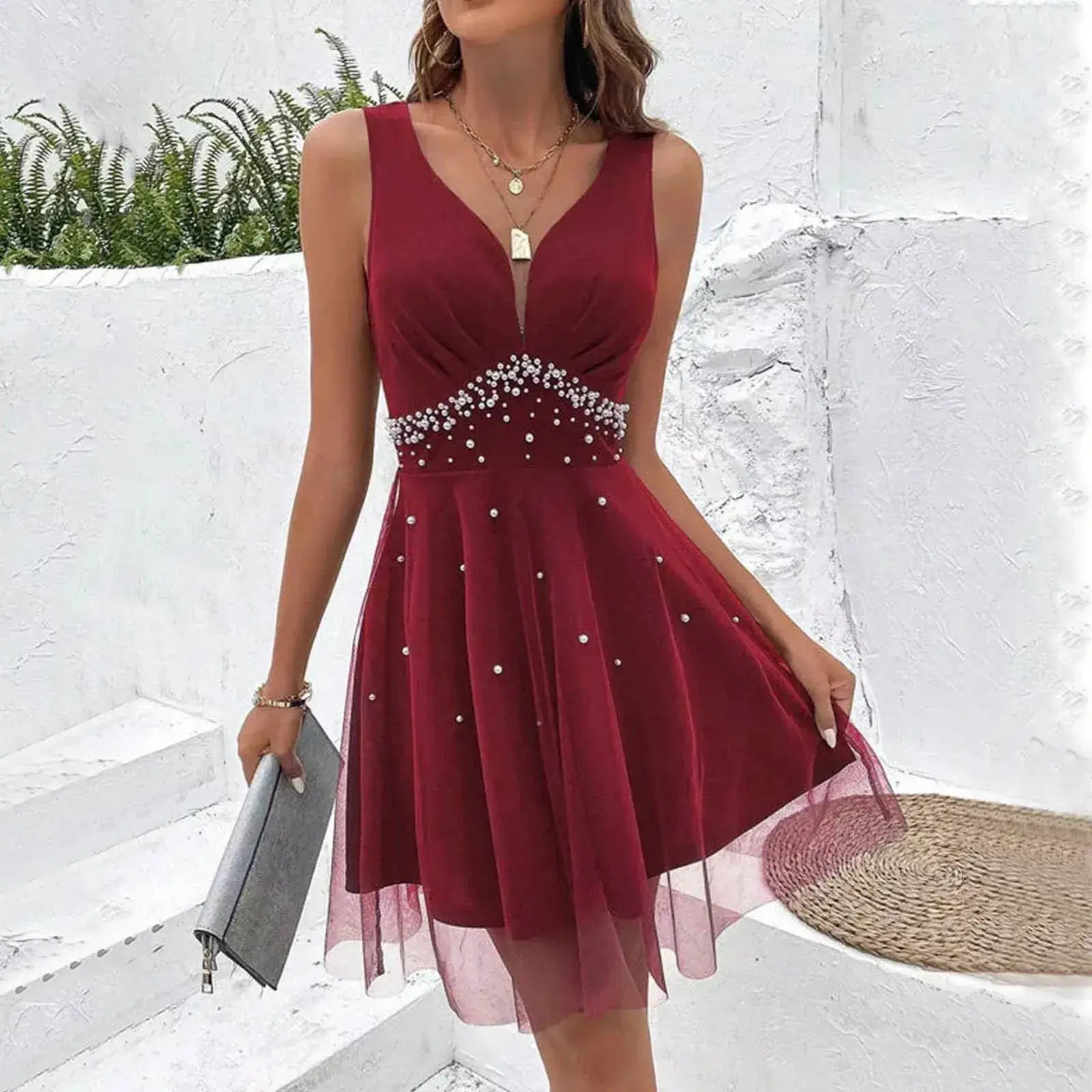 Vestido de Festa Curto Decote V Vinho, em cena externa com clutch cinza e pérolas na cintura