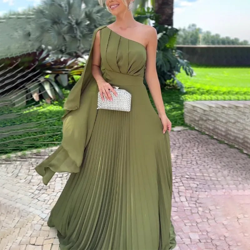 Vestido Longo Plissado Feminino Verde de Um Ombro Só em cena externa, visto de frente com clutch prateada e saia plissada