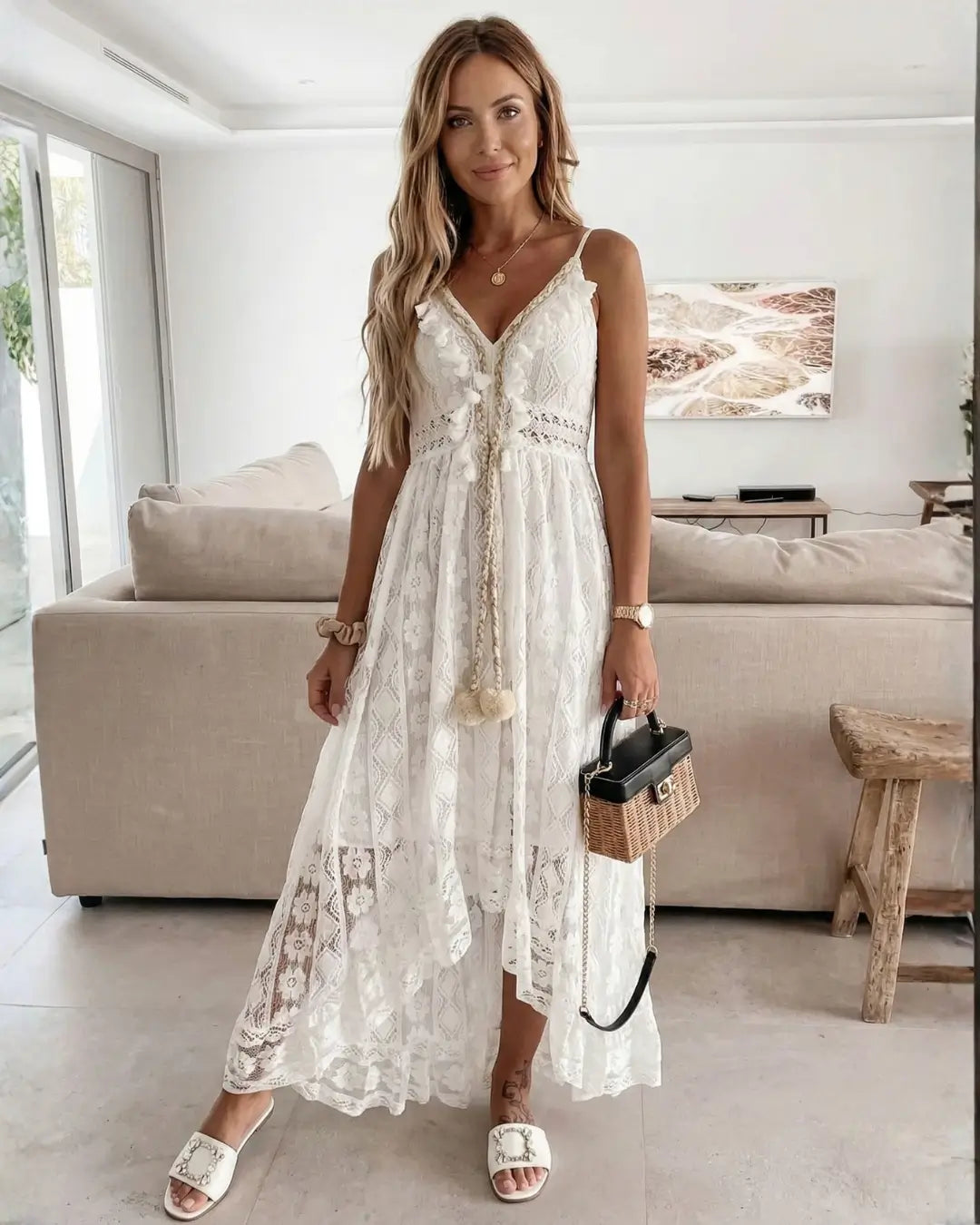 Vestido Feminino Longo de Renda Off White Estilo Boho Chic visto de frente, com alças finas, tassel na cintura e rasteira branca