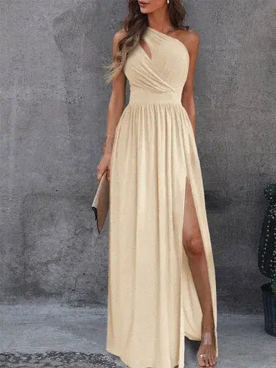 Vestido Longo Um Ombro Só com Fenda na cor champagne, visto de frente com fenda alta e clutch nude