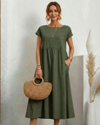 Vestido Midi Verde Oliva em Linho e Algodão visto de frente, com bolsa de palha, colares sobrepostos e bolsos laterais