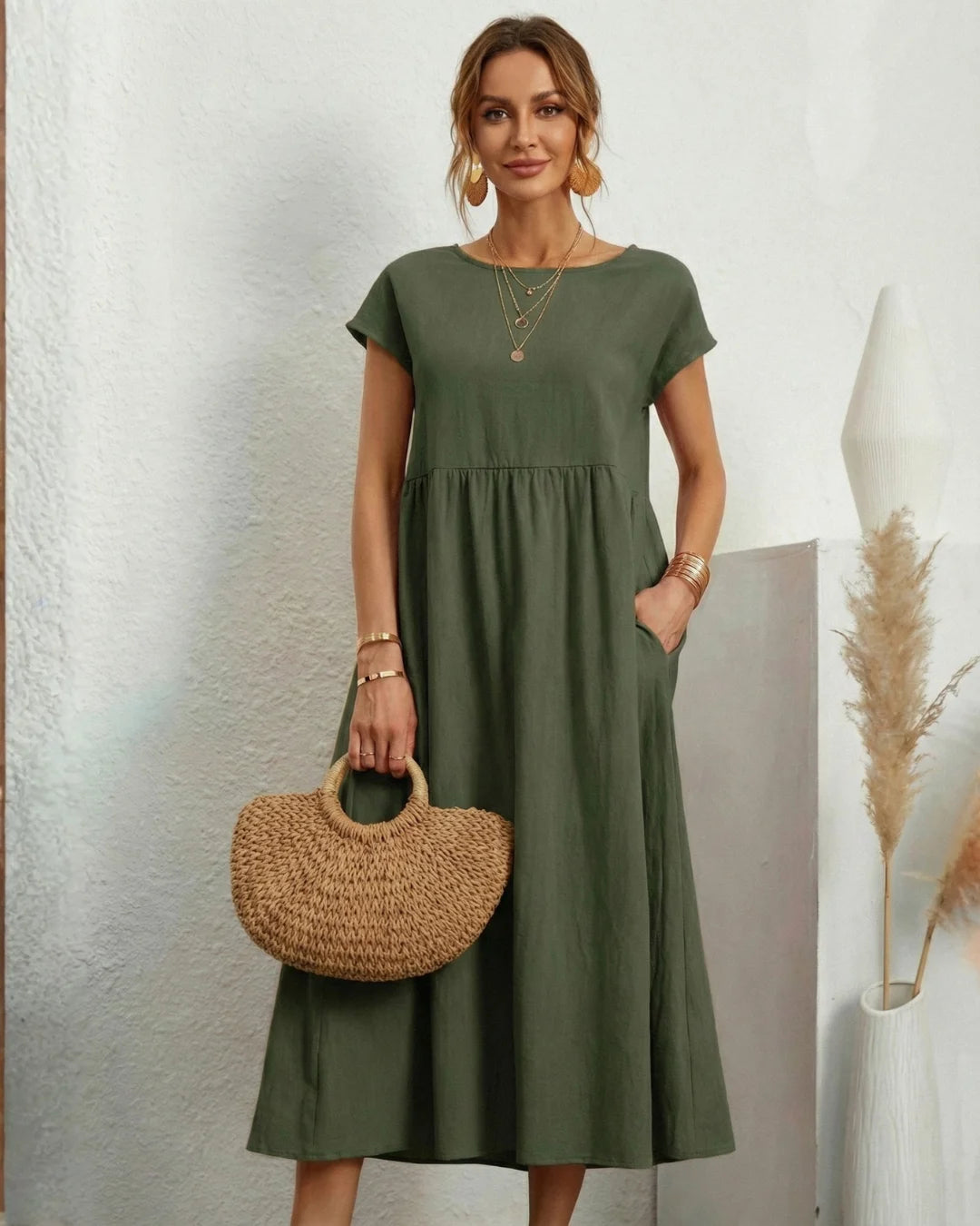 Vestido Midi Verde Oliva em Linho e Algodão visto de frente, com bolsa de palha, colares sobrepostos e bolsos laterais