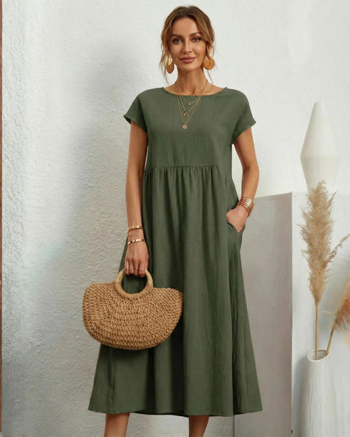 Vestido Midi Verde Oliva em Linho e Algodão visto de frente, com bolsa de palha, colares sobrepostos e bolsos laterais